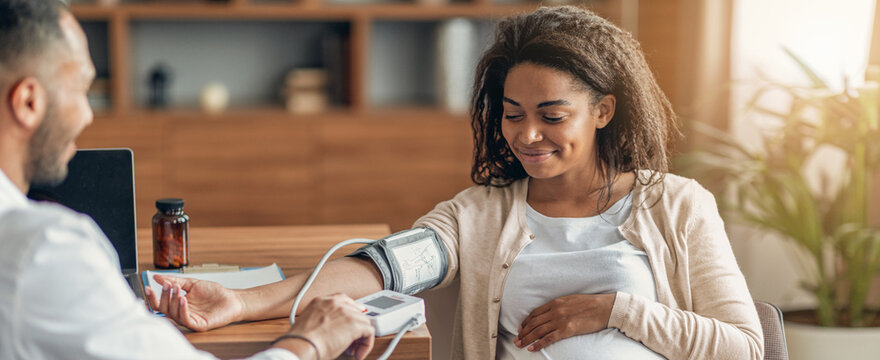 Happy Emotion Displayed By Pregnant Black Woman Receiving Blood Pressure Check From Healthcare Professional In Modern Clinic Setting. Focused On Ensuring Health And Wellbeing During Pregnancy.