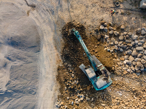 Aerial view of an excavator working on a rocky construction site with piles of gravel and dirt in Karanglewas, Central Java, Indonesia.