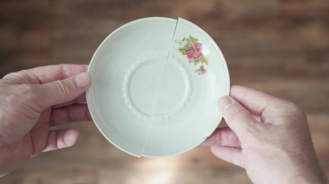 Hands hold two halves of a broken porcelain plate