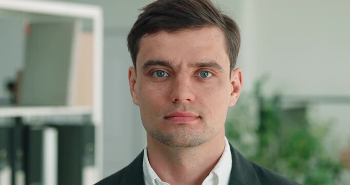 Portrait of serious Caucasian businessman in bright office keeps direct steady gaze. Man faces forward while holds composed expression during formal work moment
