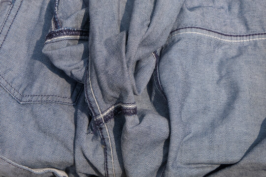 Crumpled light blue denim fabric texture with visible stitching and natural folds. Versatile textile background for fashion, apparel, clothing, and material design concepts