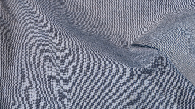 Crumpled light blue denim fabric macro texture with visible folds and woven fibers. Versatile textile background for fashion, apparel, material, and design concepts