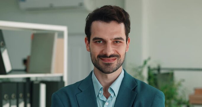 Portrait of confident Hispanic businessman in blue jacket shows steady smile. Bearded businessman crosses arms as looks ahead with relaxed authority at work