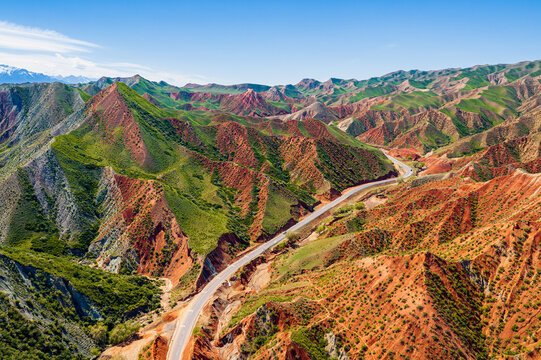 Winding road through eroded red and green mountain terrain in Xinjiang, China, offering commercial imagery for travel, geology, and tourism.