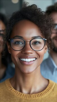 A joyful woman with a radiant smile and glasses. She is wearing a yellow top and stands in front of a blurred background. Her cheerful expression conveys a sense of positivity and approachability.