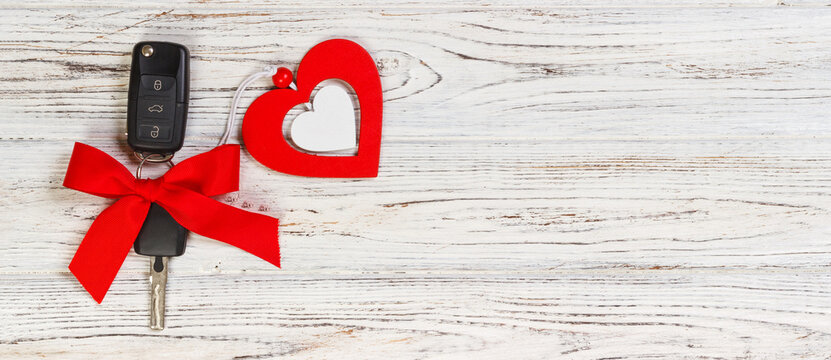Car key with a red ribbon adn a heart on white wooden table. Giving present or gift for valentine's day or christmas
