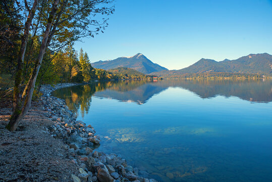 Shady shore of lake Walchensee with trees and rocks. reflecting mountains in the water