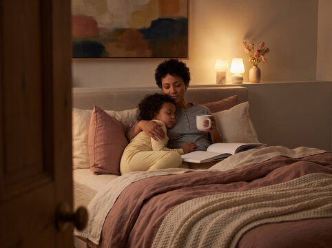 Parent and young child resting in bed with a book viewed through a doorway, representing family bonding and comforting bedtime routines.