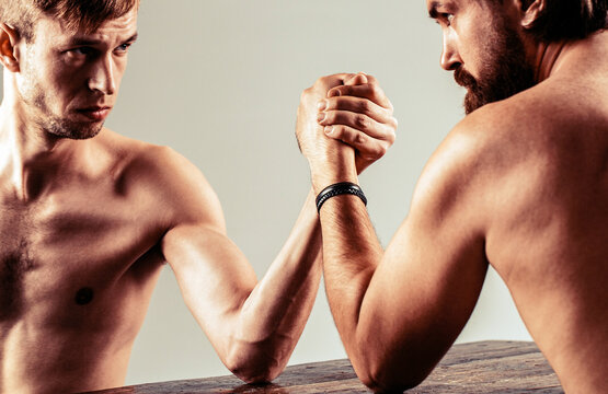 Arms wrestling thin hand, big strong arm. Strong and weak, unequal match. Heavily muscled bearded man arm wrestling a puny weak man