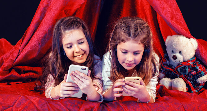 Sisters with telephone. Toddler girls lies on blanket in play tent watching cartoon on tablet with interest, telephone