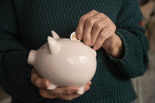 Senior Woman Putting Coin into Piggy Bank, Saving Money Concept