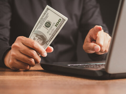 Person Holding Cash and Pointing at Camera Beside Laptop