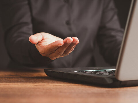 Person Extending Open Palm Beside Laptop at Desk
