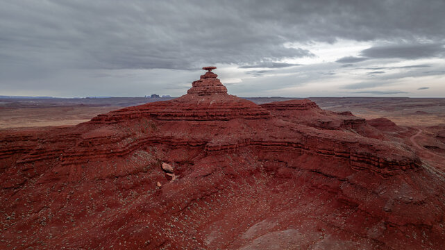 Aerial view of the iconic Mexican Hat rock formation surrounded by red sandstone desert landscape under a cloudy sky in Moab, Utah, United States.