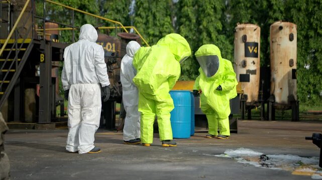 Hazmat workers in protective suits handle a chemical container during hazardous material response training at an industrial facility