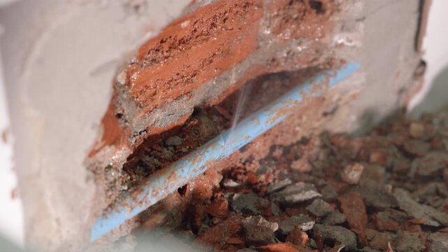 Exposed plumbing pipe inside a cracked wall reveals hidden home maintenance problems, water leakage, moisture damage, corrosion, renovation work, and the need for professional repair.
