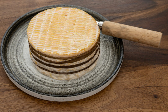 Livarot, French washed-rind cheese from Normandy, bound with sedge grass bands and featuring olden-orange rind, creamy texture and complex flavor, authentic French dairy heritage.