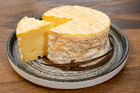 Livarot, French washed-rind cheese from Normandy, bound with sedge grass bands and featuring olden-orange rind, creamy texture and complex flavor, authentic French dairy heritage.