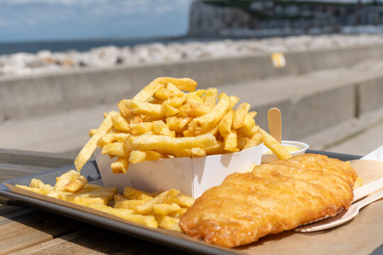 Fish and chips on Le Treport promenade &mdash; golden battered cod with mountain of french fries, seaside flavors enjoyed outdoors by the harbor in Normandy, France