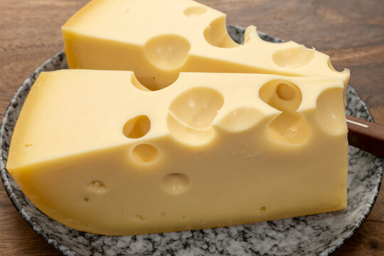 French Emmental cheese from Savoie Alps with large holes, traditional fermentation and aging, pale golden color, firm creamy texture, French food
