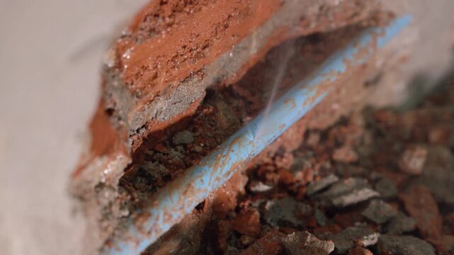 Exposed plumbing pipe inside a cracked wall reveals hidden home maintenance problems, water leakage, moisture damage, corrosion, renovation work, and the need for professional repair.