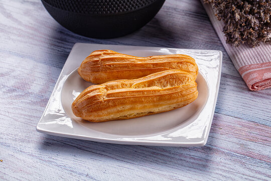 Two golden eclairs on white plate with rustic wooden background