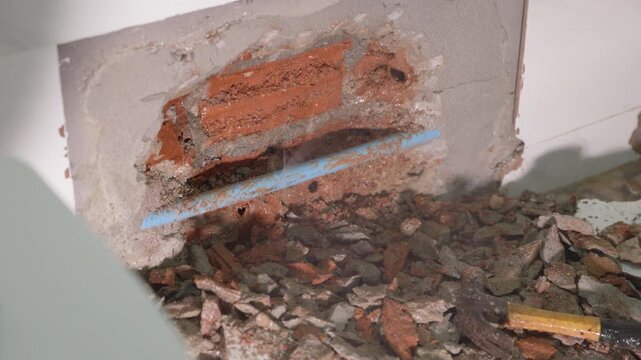 Close-up of a leaking water pipe inside a damaged wall, showing plumbing failure, moisture, cracked plaster, water damage, corrosion, and the need for urgent home maintenance and repair.