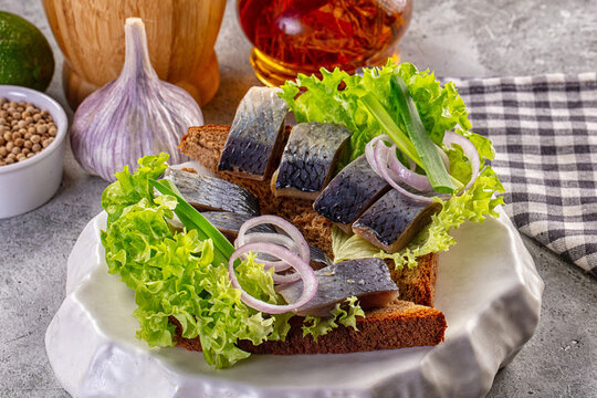 Open faced sandwich with herring slices lettuce and red onion on rye bread