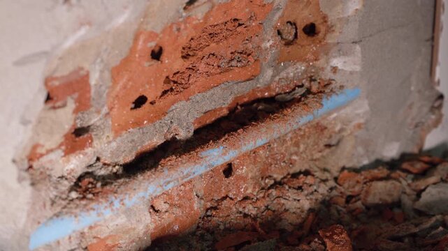 Close-up of a leaking water pipe inside a damaged wall, showing plumbing failure, moisture, cracked plaster, water damage, corrosion, and the need for urgent home maintenance and repair.