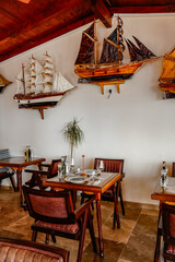 Traditional restaurant interior with decorative sailing ship models and wooden dining furniture © Liana