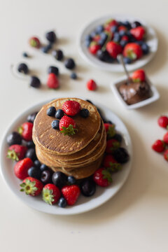 Sweet toddler child, boy, eating american pancakes with strawberries, cherries and blueberries, topped with syrup and drinking fresh orange juice