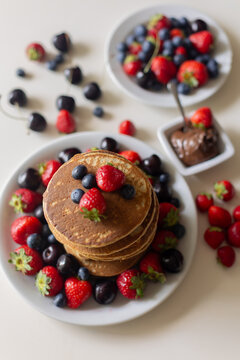 Sweet toddler child, boy, eating american pancakes with strawberries, cherries and blueberries, topped with syrup and drinking fresh orange juice