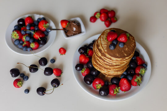 Sweet toddler child, boy, eating american pancakes with strawberries, cherries and blueberries, topped with syrup and drinking fresh orange juice