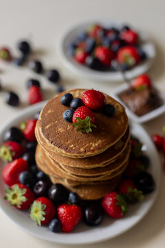 Sweet toddler child, boy, eating american pancakes with strawberries, cherries and blueberries, topped with syrup and drinking fresh orange juice