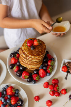 Sweet toddler child, boy, eating american pancakes with strawberries, cherries and blueberries, topped with syrup and drinking fresh orange juice