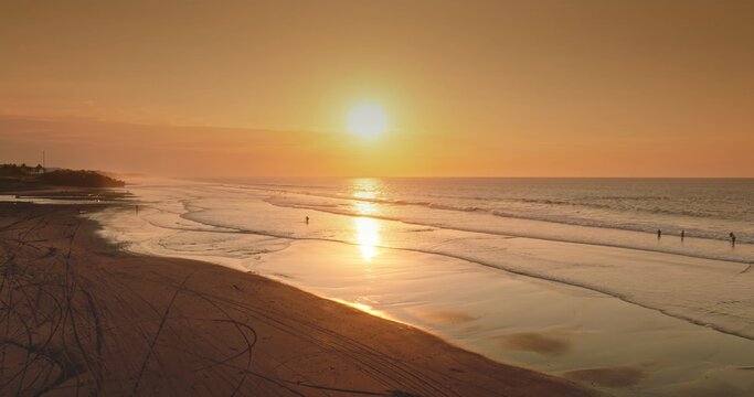 Aerial view of a serene beach at sunset with golden light reflecting on the wet sand and gentle waves rolling onto the shore in Bali, Indonesia.