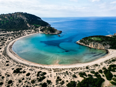 Aerial view of Voidokilia Beach with its iconic crescent-shaped bay, turquoise waters, sandy dunes, and surrounding hills in Greece.