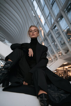 futuristic portrait of stylish person in modern architectural interior, elegant blonde model in black turtleneck against curved white architecture, sophisticated portrait with futuristic architecture