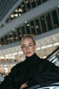 futuristic portrait of stylish person in modern architectural interior, elegant blonde model in black turtleneck against curved white architecture, sophisticated portrait with futuristic architecture