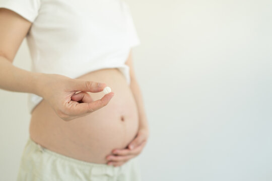 Pregnant woman holding dietary supplement pill against white background. Maternity prenatal care concept.