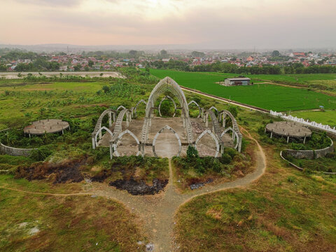 Aerial view of the Masjid Agung Purwokerto, featuring its distinctive crescent-shaped architectural arches set amidst lush green fields in Purwokerto, Central Java, Indonesia.