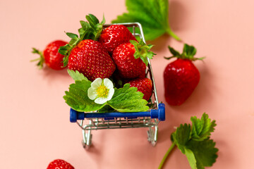 Fresh strawberries in miniature shopping cart on pink background © Peredniankina