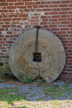 Vertical view of a large old millstone leaning against a red brick wall in Germany
