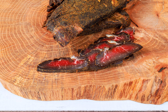 Beef jerky slices on wooden surface with large piece of whole cured beef