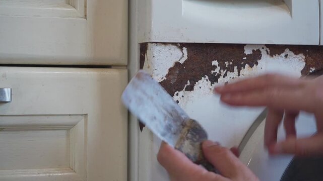 Scraping rust off washing machine with spatula close up, Cleaning corrosion and damaged paint from washing machin