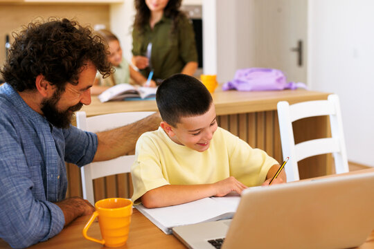 Father and son studying together at home learning and doing homework. Mother and daughter also studying in background
