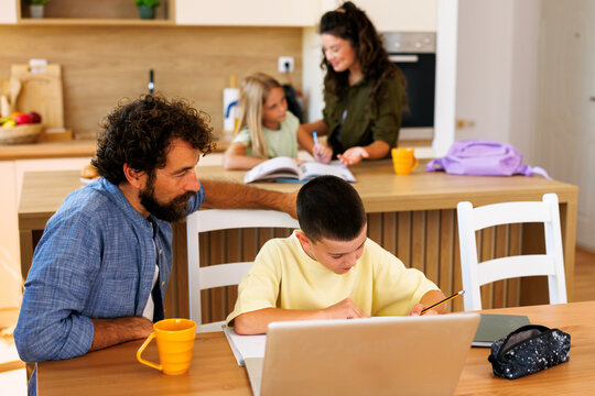 Family members supporting children with schoolwork and online learning, studying together in a modern kitchen environment