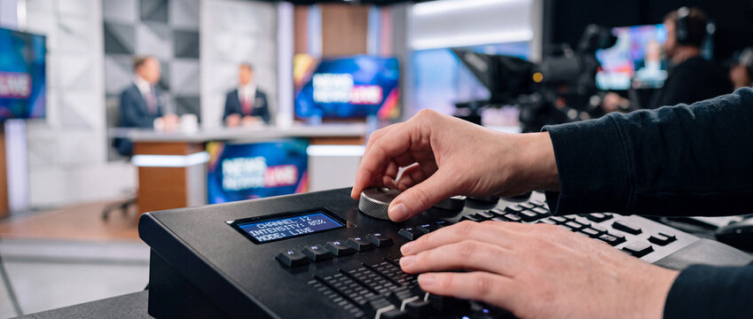 Broadcast control room technician adjusting mixing console during live news production in tv studio