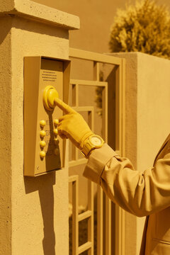 Person in yellow gloves pressing a doorbell button