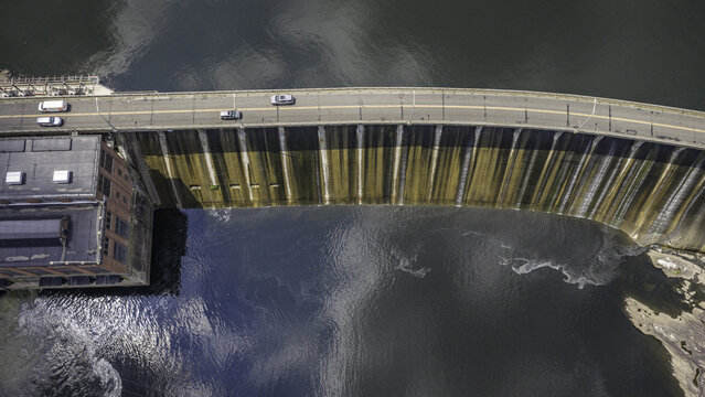 Aerial view of the Stevenson Generating Station hydroelectric dam with a roadway crossing the top and water flowing down the concrete wall in Monroe, CT, United States.